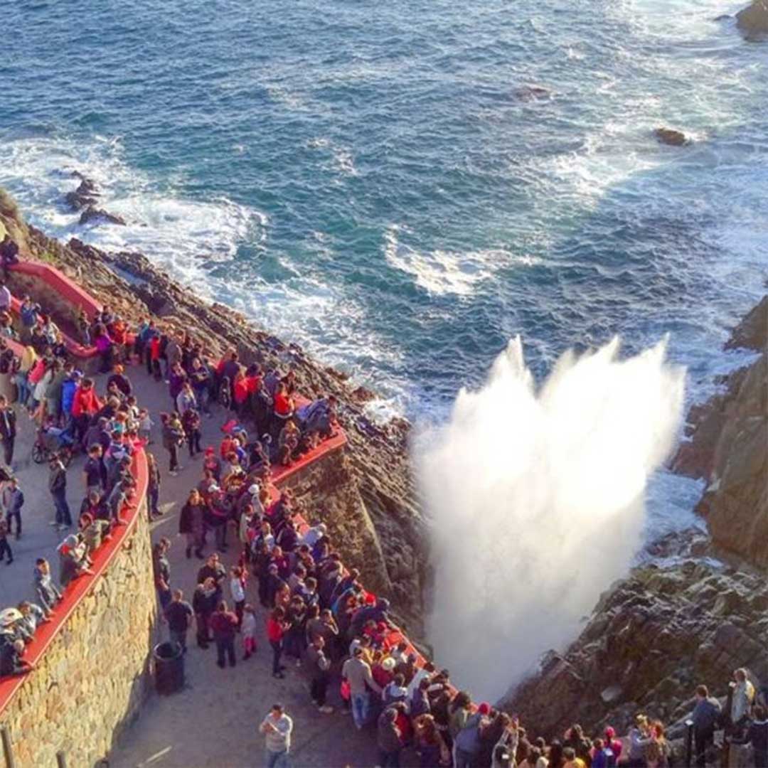 Tourists enjoying a private La Bufadora Ensenada tour with the marine geyser exploding and local vendors in the background.