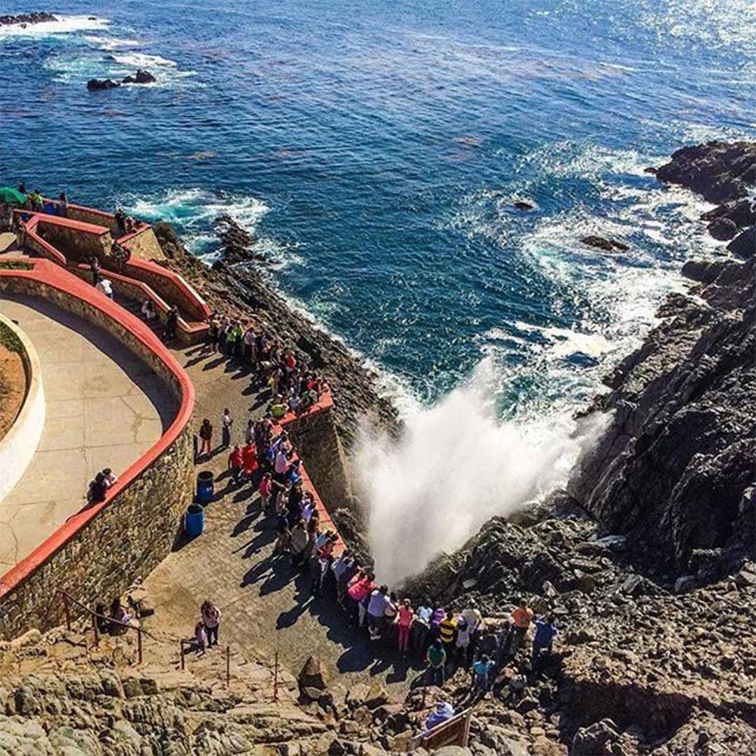 Turistas disfrutando de un tour privado a La Bufadora en Ensenada con el géiser marino explotando de fondo.